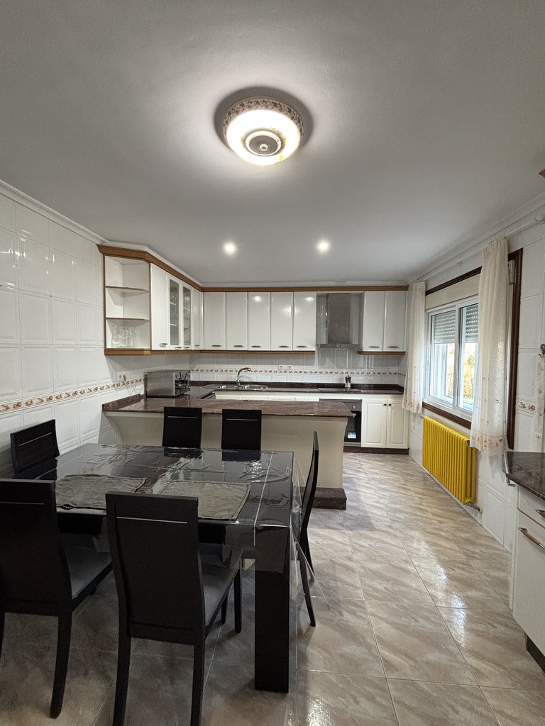 Cocina-comedor amplia con muebles blancos, encimera de granito y mesa de cristal para seis personas