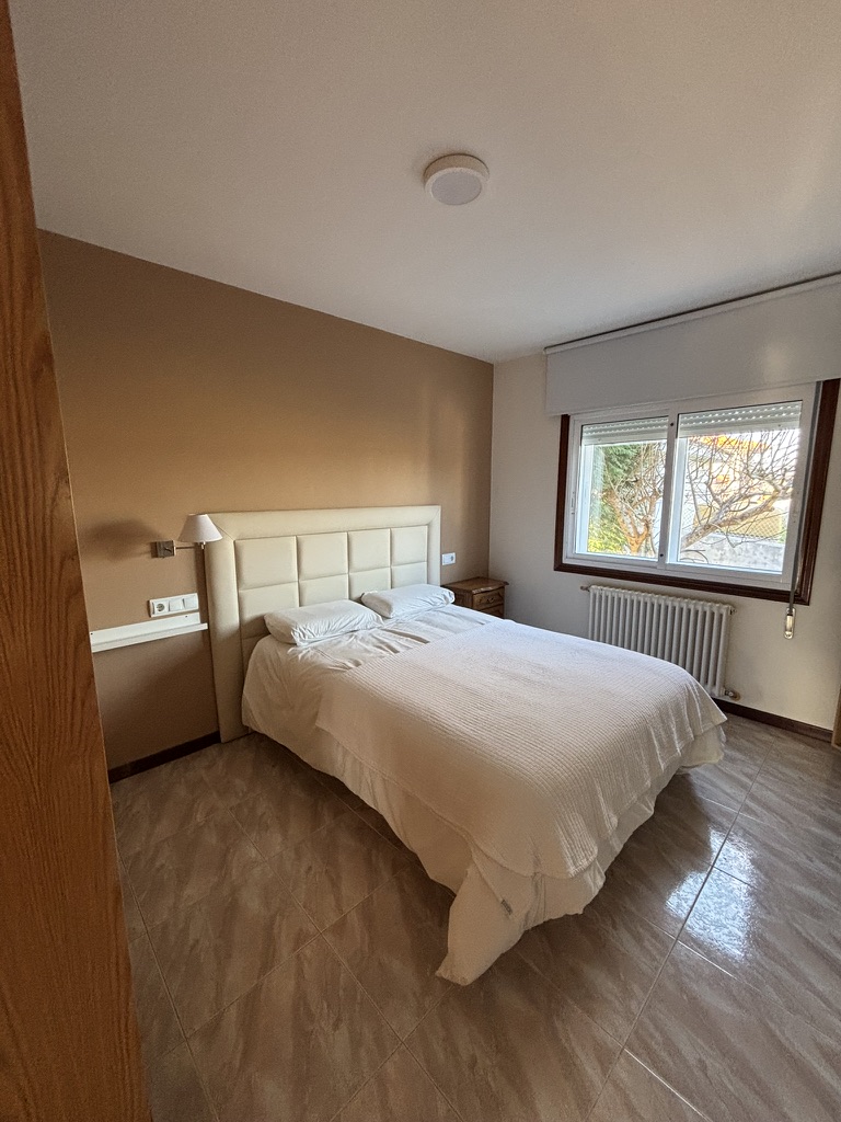 Dormitorio secundario con cama de matrimonio, cabecero tapizado en beige y abundante luz natural