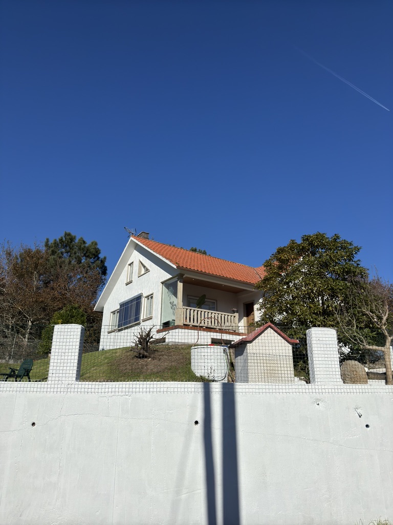 Fachada exterior de Enriba Do Portal: casa unifamiliar con tejado rojo, balcón de granito y vegetación gallega